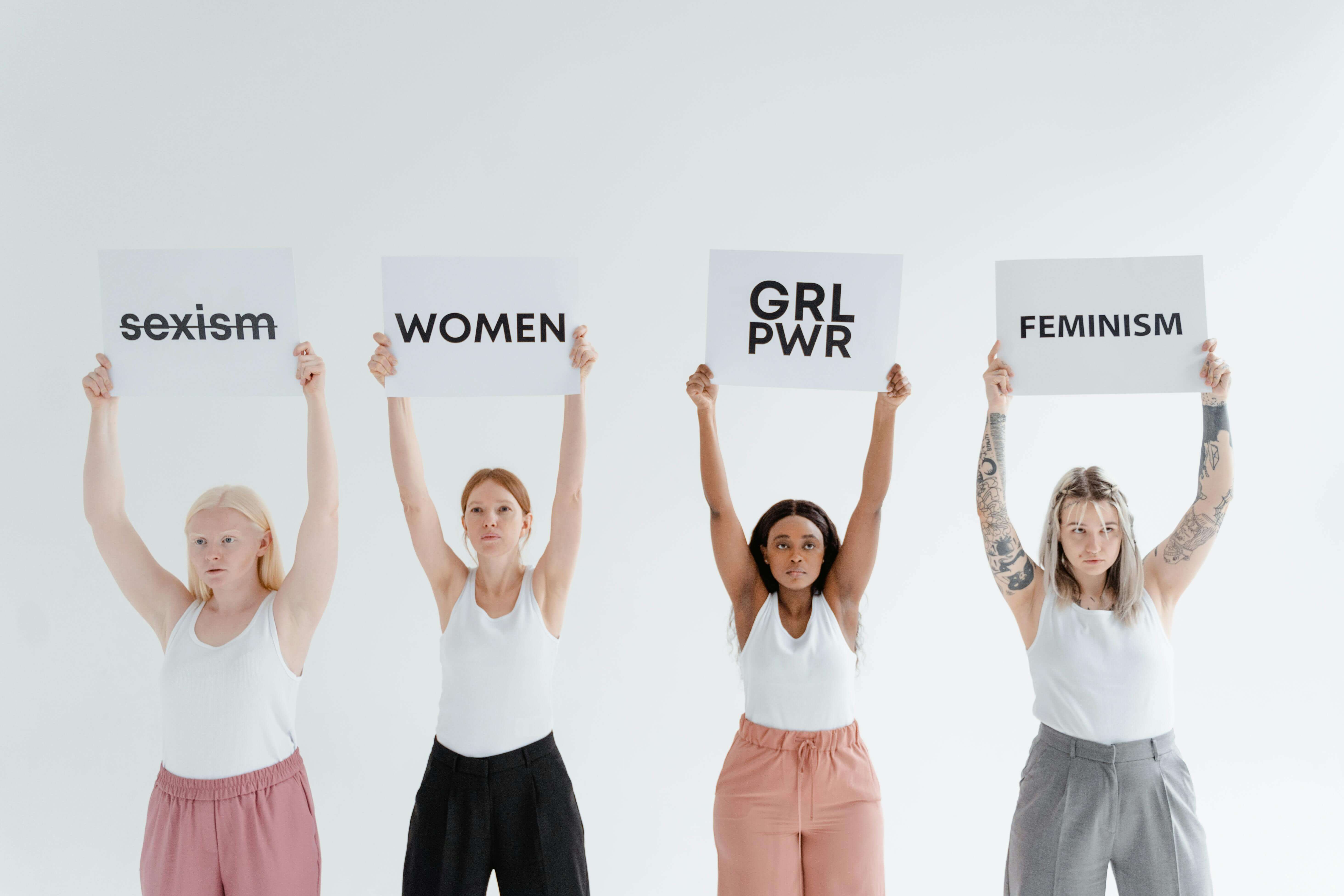 Women holding signs that say girl power, feminism, and stop sexism.